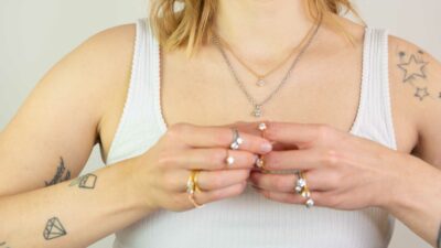 Dekoltée und Hände einer Frau mit Kettenanhänger und Ringen aus fairem Gold als zeitloses Layering in der Chaton Kollektion von Jan Spille Schmuck vom Goldschmied