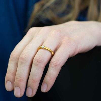 Frau zeigt ihre Hand mit gelb goldenem Verlobungsring mit kleinem Stein aus der Kordel-Kollektion von Jan Spille Wir verwenden nur Fairmined Eco Gold mit ethischem Naturdiamanten
