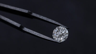 Ein geschliffener Labor Diamant wird zwischen einer Zange präsentiert