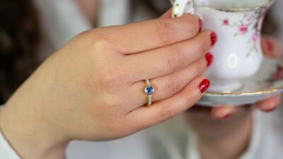Frau trinkt Tee aus Tasse und trägt klassischen Verlobungsring echtgold im Pavé mit konfliktfreien Naturdiamanten und Fairtrade Saphir