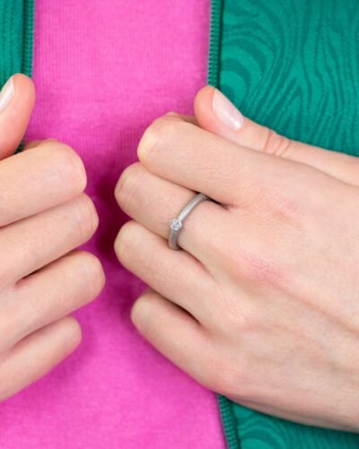 Frau mit grüner Jacke und pinkem Shirt zeigt runden Verlobungsring aus Recycling Weissold mit Ethical Diamond Stein in Zargefassung von Jan Spille aus Hamburg