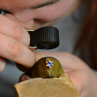 goldener verlobungsring mit blauem stein wird unter der lupe genau betrachtet um qualitätsansprüche von jan spille zu erhalten