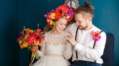braut mit buntem blumenkranz und blumenstrauß nebenbräutigam betrachten ihre trauringe mit hammerschlag textur