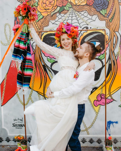 Bunte Hochzeit, Mann hebt seine Braut hoch vor einem bunten Graffiti sie tragen eheringe von jan spille