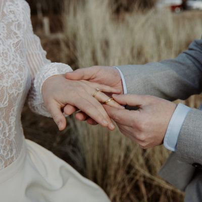 Ehepaar heiratet auf dem Land, Mann steckt seiner Frau einen Trauring von Jan Spille Schmuck auf den linken Ringfinger zum Verlobungsring