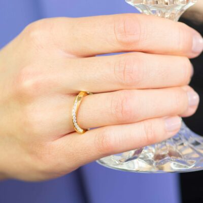 Frau trägt zierlicher Verlobungsring gedreht aus Fairtrade Gold gewickelt mit fairen Diamanten von Jan Spille und hält ein Sektglas