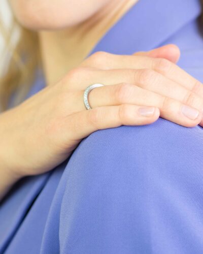 Eine Frau fasst sich an die Schulter und zeigt zierlichen weißgold Verlobungsring gedreht der Twister-Kollektion aus Fairtrade Gold gewickelt mit fairen Diamanten von Jan Spille Hamburg