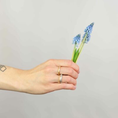 Frau trägt Wickelringe Verlobungsringe gedreht aus der Twister-Kollektion aus Fairtrade Gold und Fairtrade Naturdiamanten und hält Frühlingsblumen