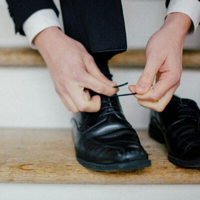 Bräutigam bindet sich seine schwarzen schuhe bei hochzeit in hamburg mit nachhaltigen eheringen von jan spille
